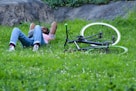 woman in blue denim shorts lying on green grass field beside black and white bicycle during