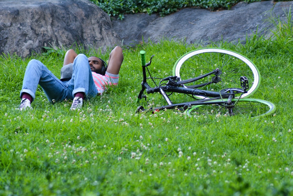 Frau in blauen Jeansshorts liegt auf grünem Rasen neben schwarz-weißem Fahrrad während