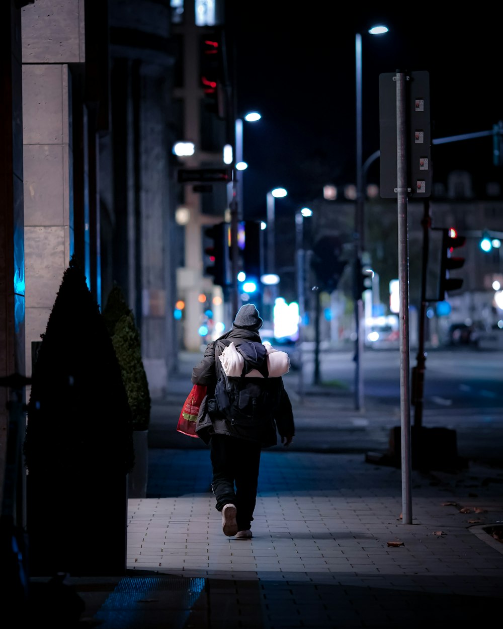 donna in giacca nera e pantaloni neri che cammina sul marciapiede durante la notte