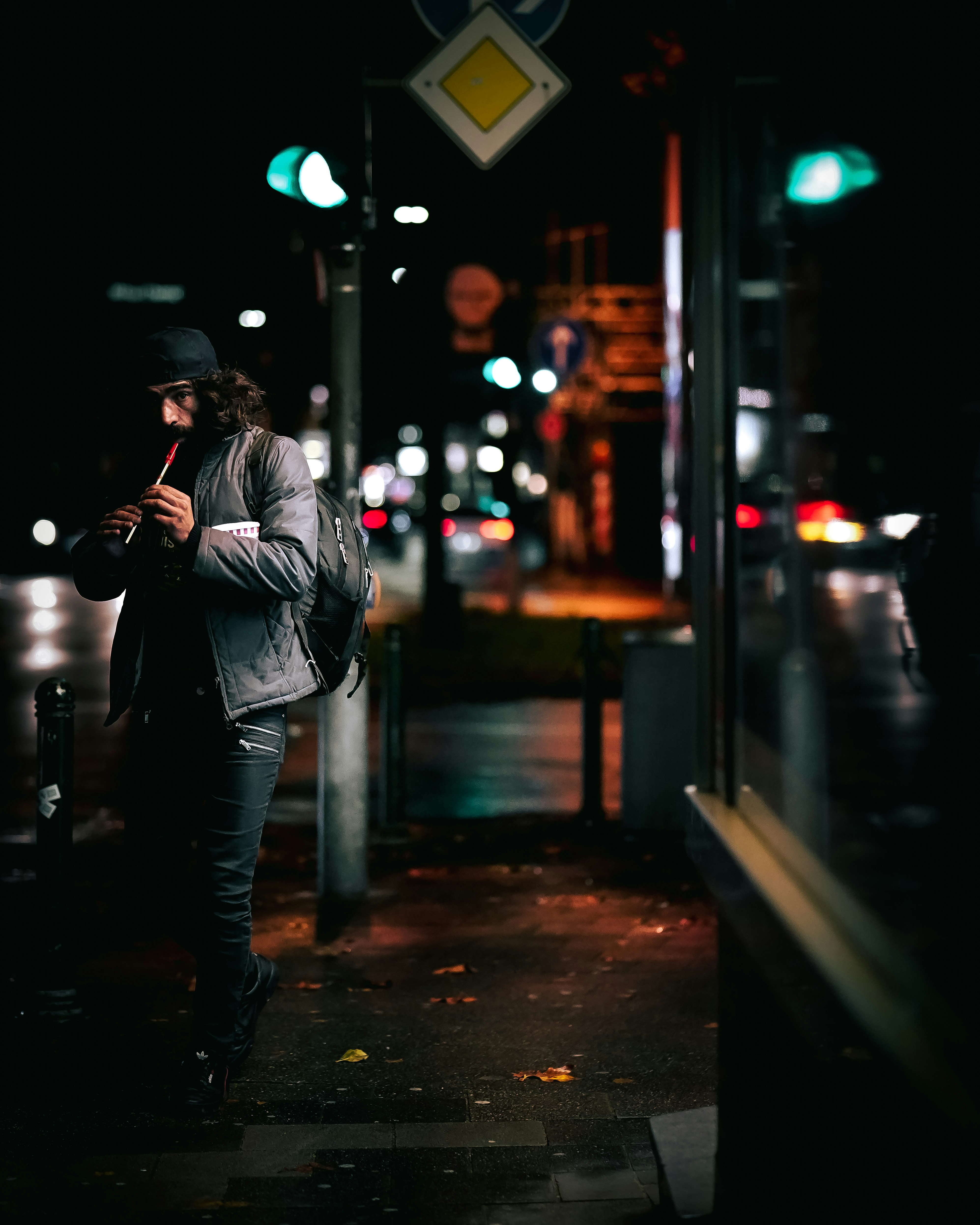 man in black leather jacket and blue denim jeans standing on sidewalk during night time
