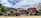 Several stacks of crushed cars in various colors are piled together in an open area, surrounded by trees under a partially cloudy sky.