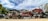 Several stacks of crushed cars in various colors are piled together in an open area, surrounded by trees under a partially cloudy sky.