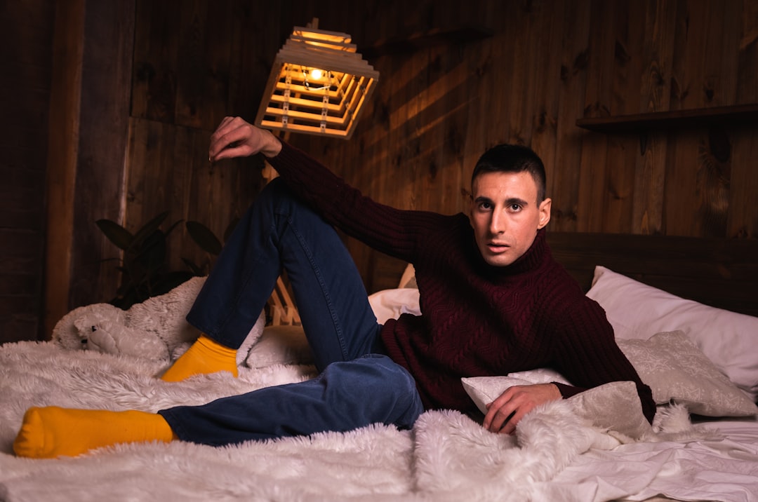 man in black sweater and blue denim jeans sitting on white fur textile