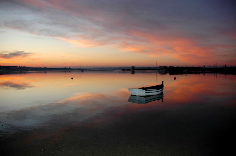 white boat on calm water during sunset