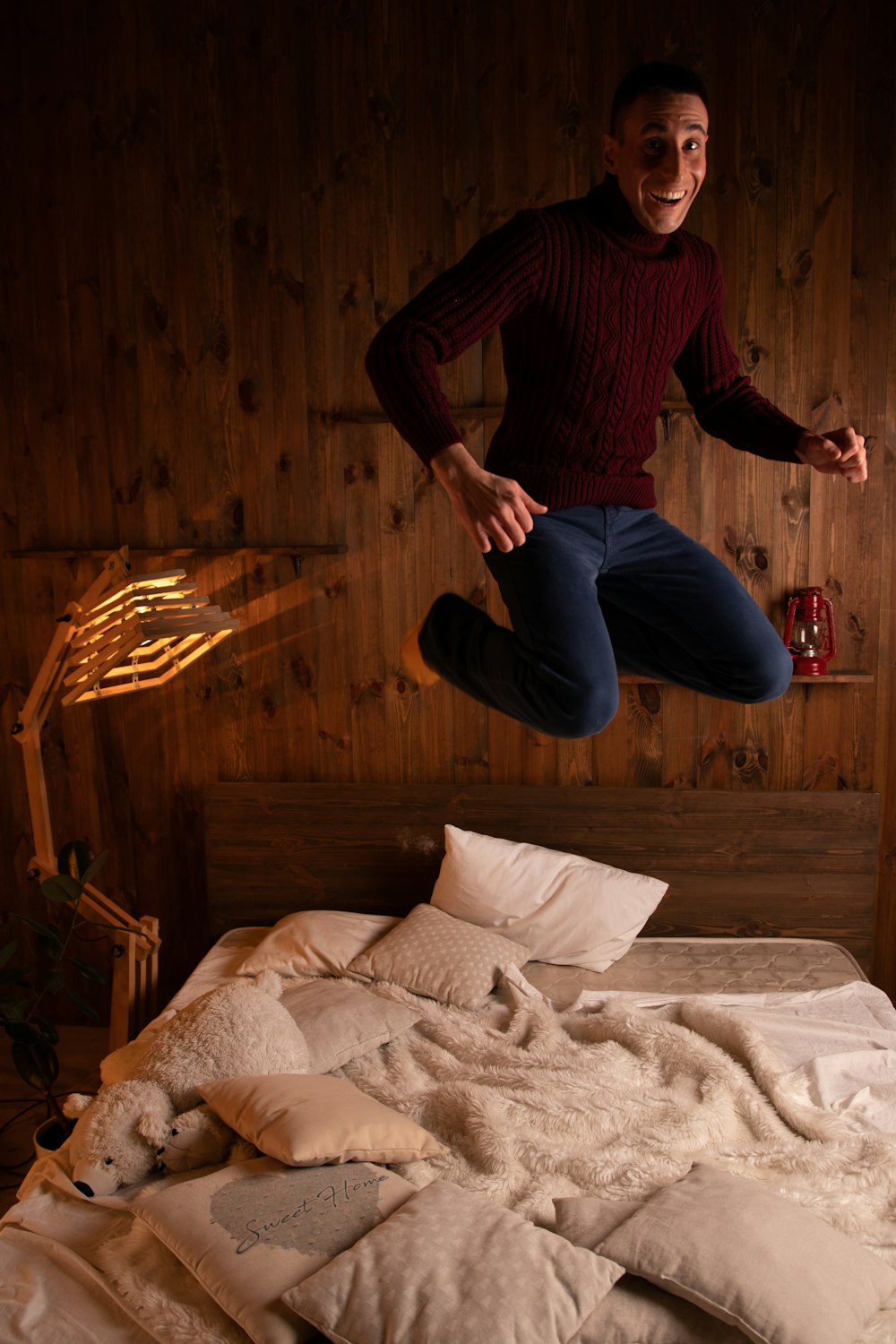 Hombre con camisa de manga larga a rayas rojas y negras y jeans de mezclilla azules saltando en la cama