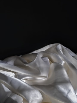 Smooth, lustrous fabric featuring a flowing, draped arrangement with graceful folds against a dark background.