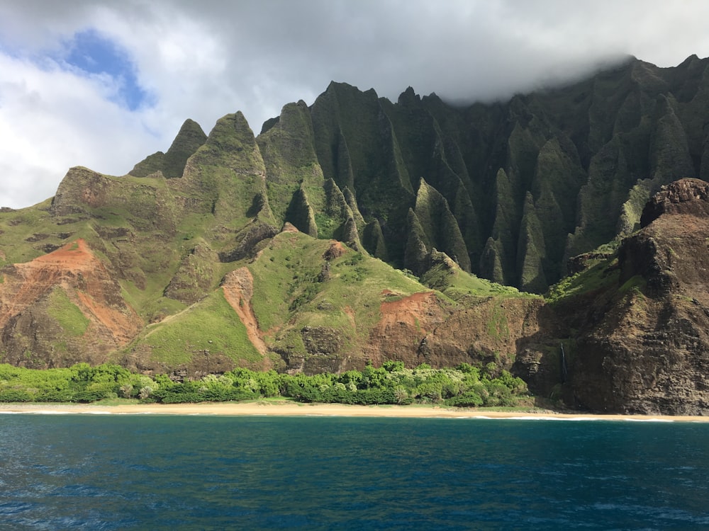 green and brown mountain beside blue sea under white clouds during daytime