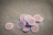 A collection of circular tokens with the Bitcoin logo lies scattered on sand. Each token features an orange circle with a white border and the symbolic Bitcoin 'B' in the center.