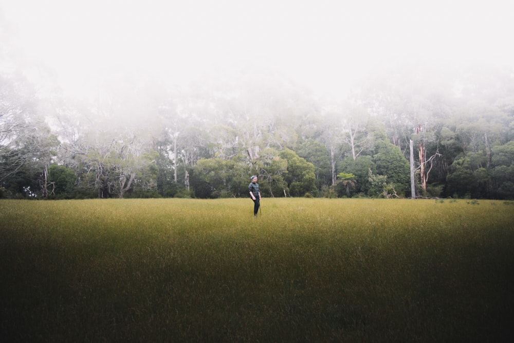 pessoa na jaqueta preta em pé no campo de grama verde durante o dia