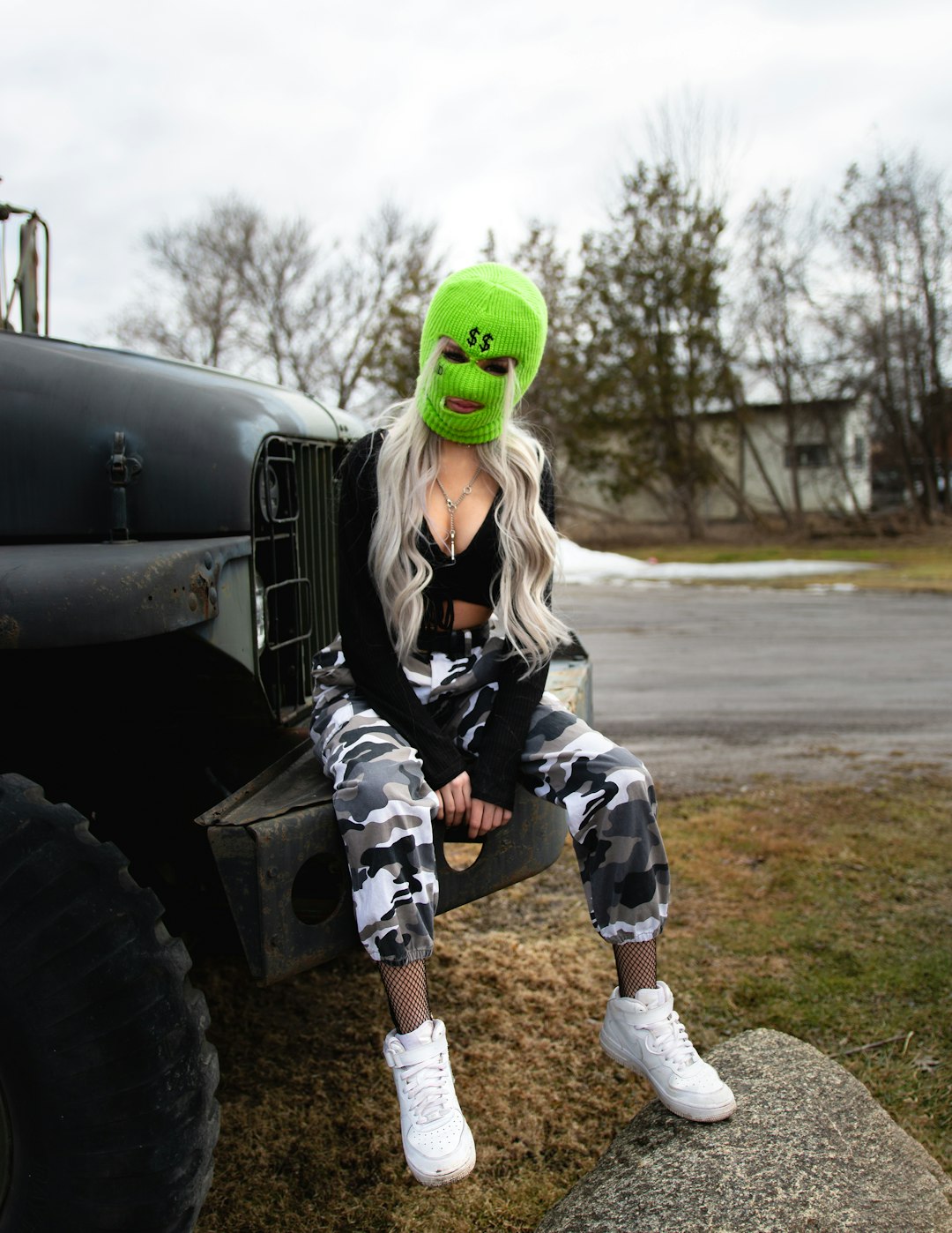 woman in green mask and black jacket sitting on gray metal tank during daytime