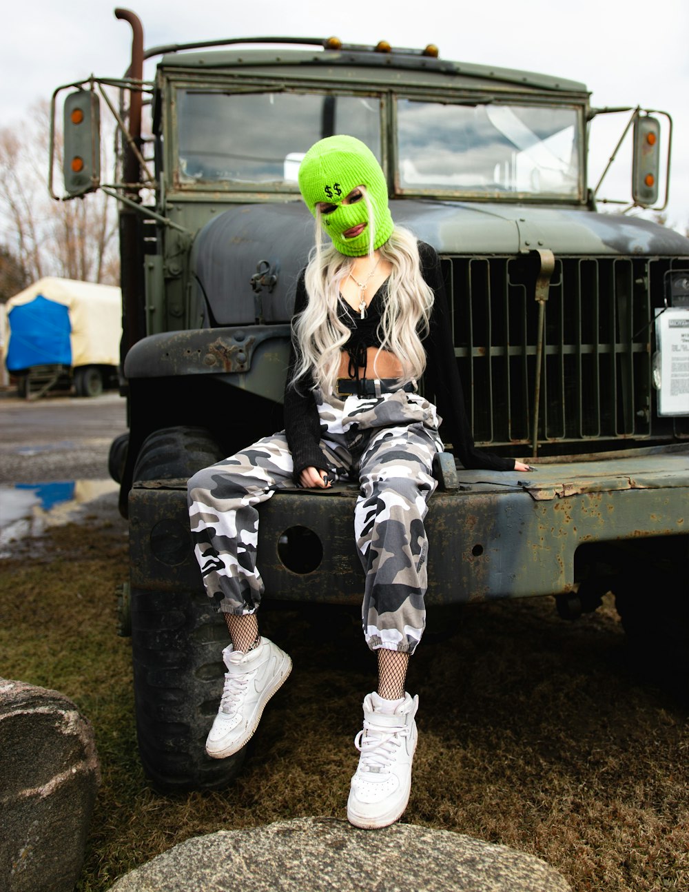 woman in black and white camouflage jacket and pants wearing green mask sitting on truck