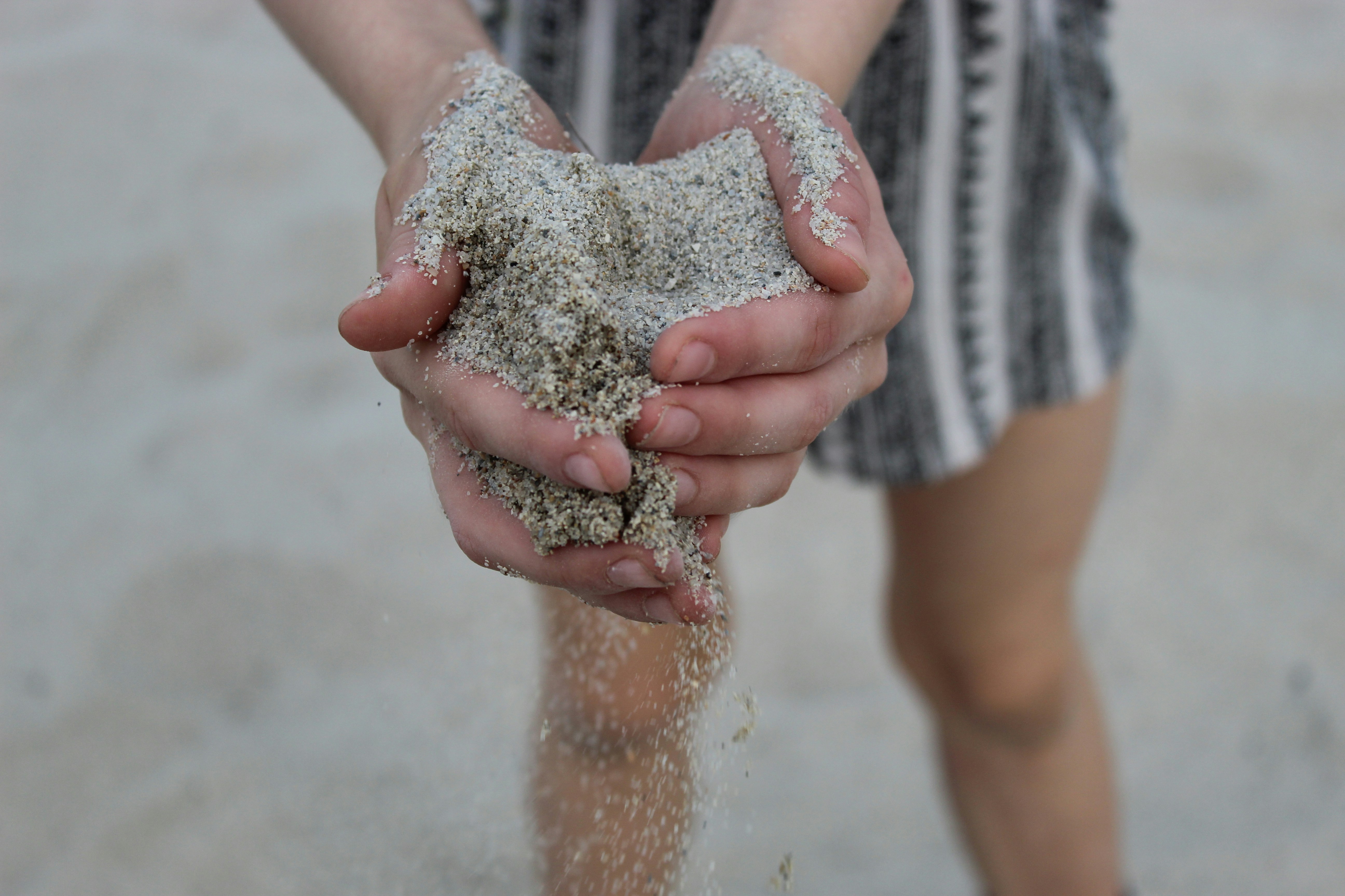 person in grey shorts with sand on hand
