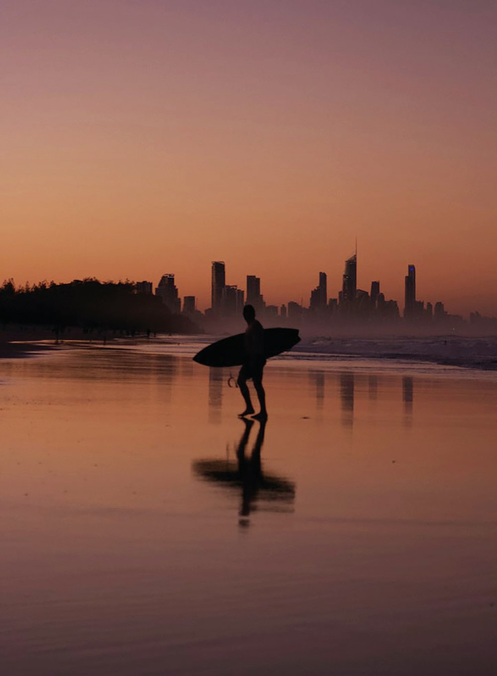 silhouette of person holding surfboard walking on beach during sunset