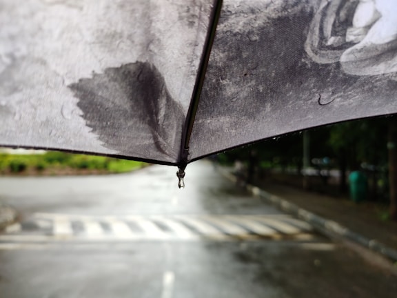 Close-up of a sleek black folding umbrella with water droplets on its canopy.
