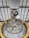 A detailed view of a complex engine or machinery component, featuring numerous metallic pipes, valves, and spherical objects. The structure is surrounded by a large yellow circular frame and is positioned against a ceiling with a grid-like pattern of beams.