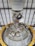 A detailed view of a complex engine or machinery component, featuring numerous metallic pipes, valves, and spherical objects. The structure is surrounded by a large yellow circular frame and is positioned against a ceiling with a grid-like pattern of beams.