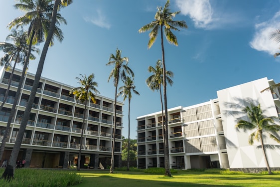 A bright, tropical motel exterior surrounded by lush palm trees and vibrant flowers under a clear blue sky.