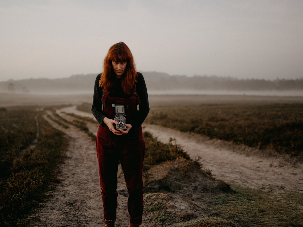 woman in black jacket and red pants standing on dirt road