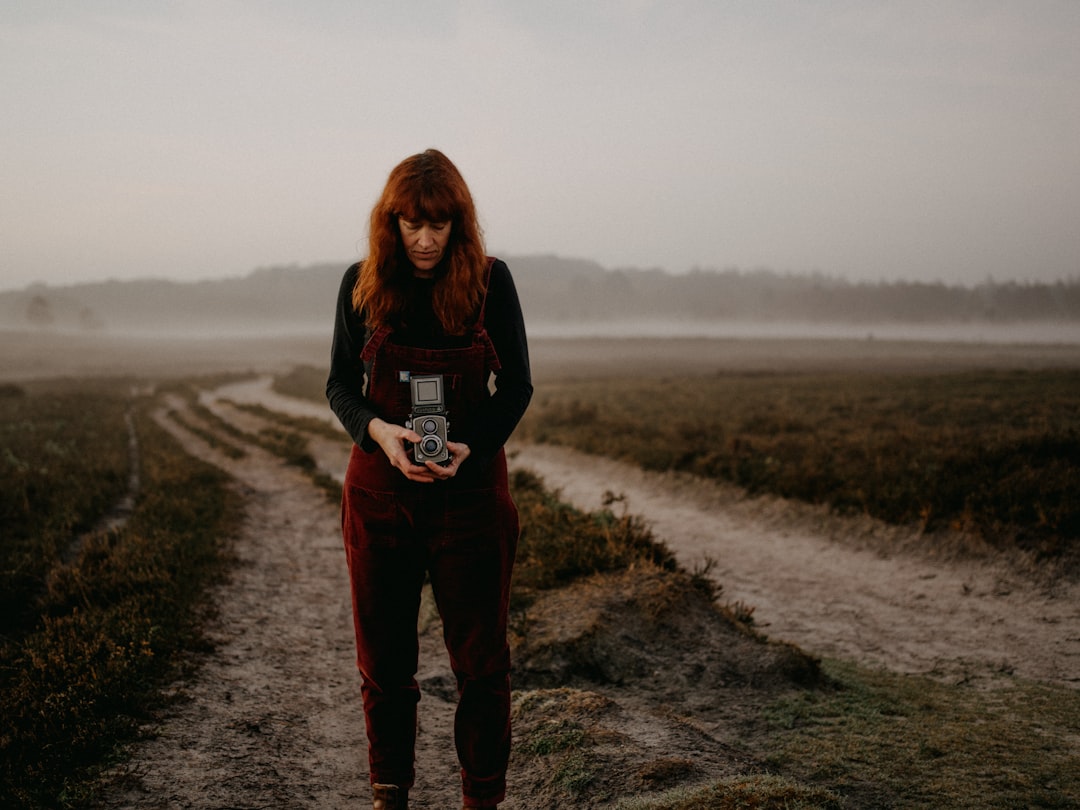 woman in black jacket and red pants standing on dirt road