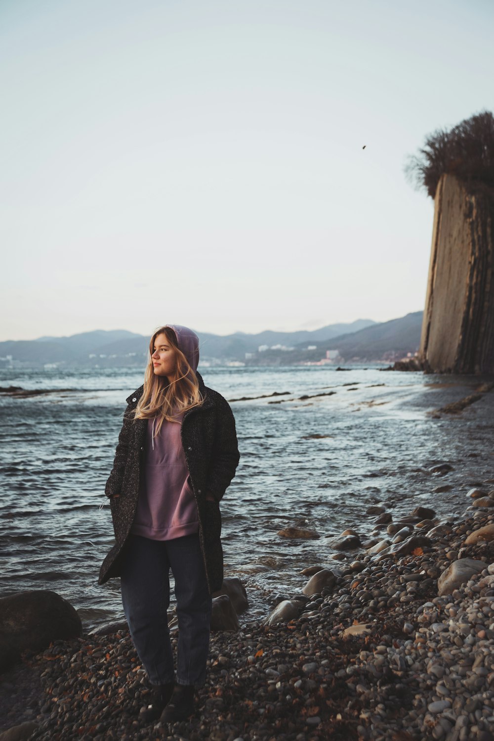 woman in purple long sleeve shirt standing on rocky shore during daytime