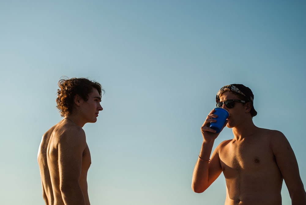 topless man wearing black sunglasses holding blue cup