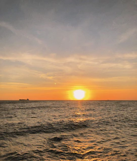 A serene cruise ship sailing under a golden sunset sky over calm ocean waters.