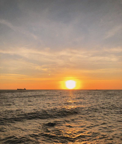 A serene cruise ship sailing under a golden sunset sky over calm ocean waters.