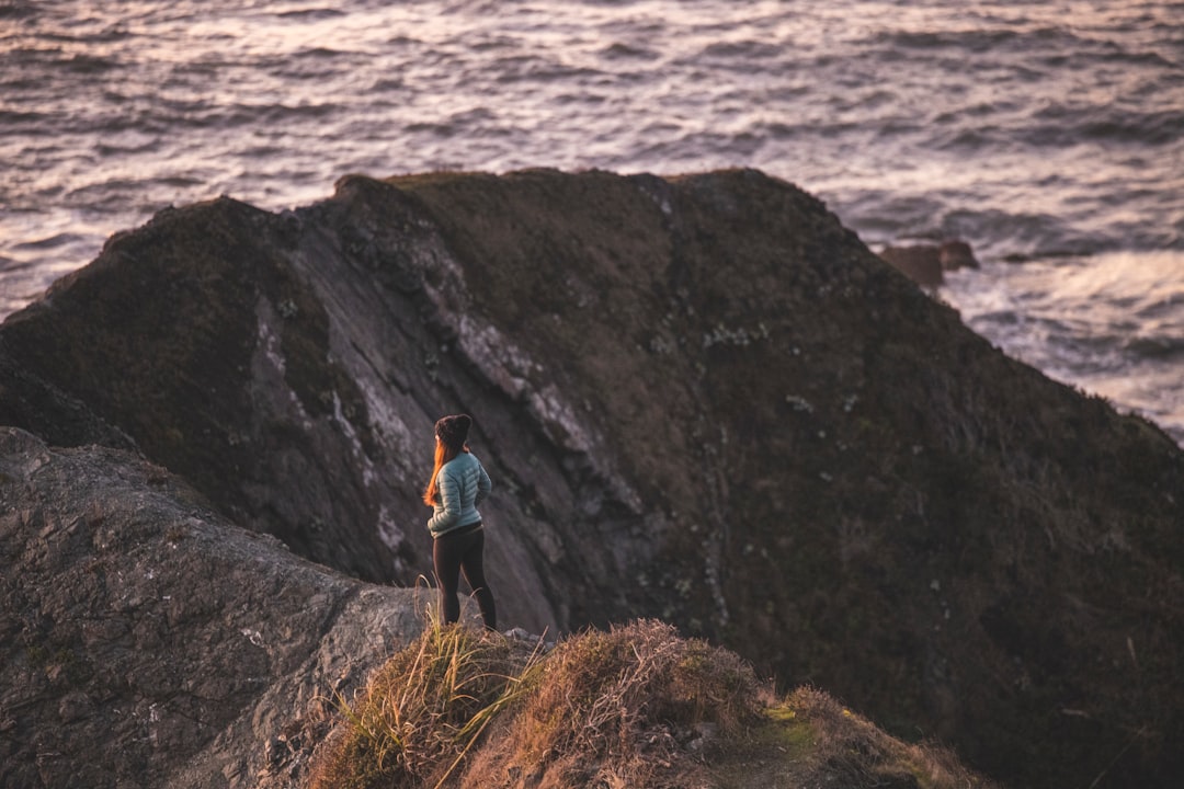 person in blue jacket standing on rock near body of water during daytime