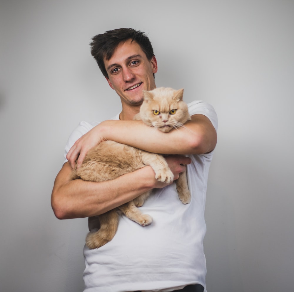 man in white crew neck t-shirt carrying brown cat