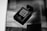 A black perfume bottle labeled 'Coco Noir Chanel Paris' is placed on an open magazine page. The page features a grayscale image of a landscape with silhouetted figures and text written in light color.