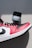 A red, white, and black sneaker is placed on a gray background near a small container labeled 'hmd'. The sneaker features a prominent swoosh logo and has a combination of leather textures.