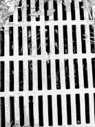 A metal grate with parallel bars covers a drain or opening. The surface appears weathered with debris and leaves scattered on top, suggesting an outdoor setting.