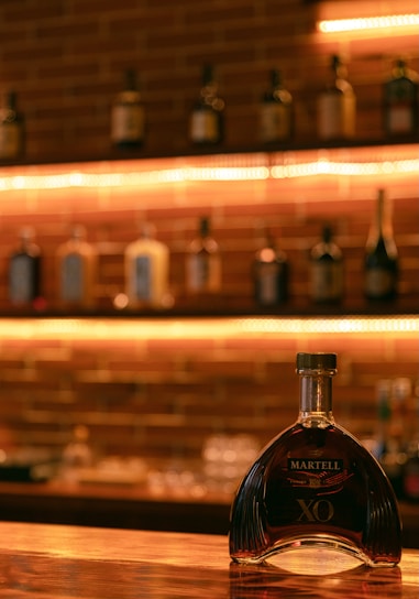 A cozy tasting room with bottles of Jean-Luc Pasquet Cognac displayed on wooden shelves.