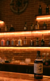 A sleek bottle of aged whisky resting on a polished oak barrel in dim, warm lighting