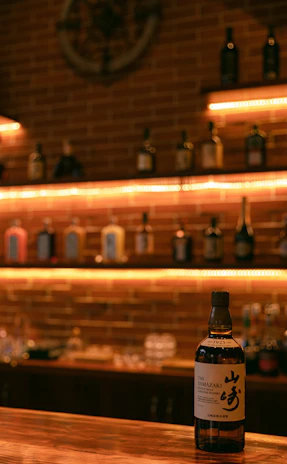 A warm, inviting whisky bar with wooden shelves lined with diverse whisky bottles, softly lit by amber lights.