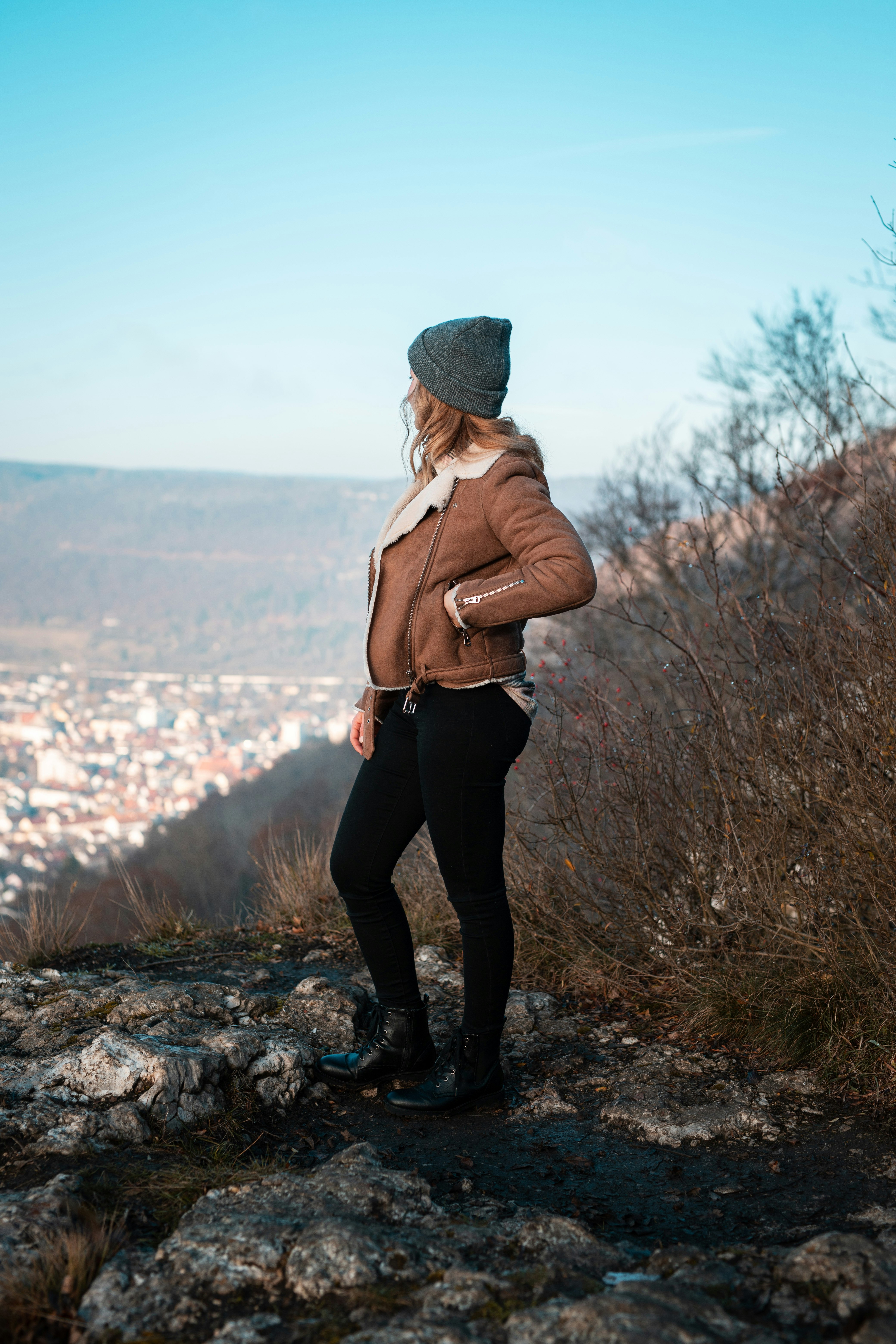 woman in brown leather jacket and black pants standing on rocky ground during daytime