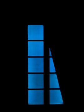 A series of rectangular and triangular blue panes arranged vertically against a black background. The shapes form a structured, abstract pattern with a modern and minimalist aesthetic.