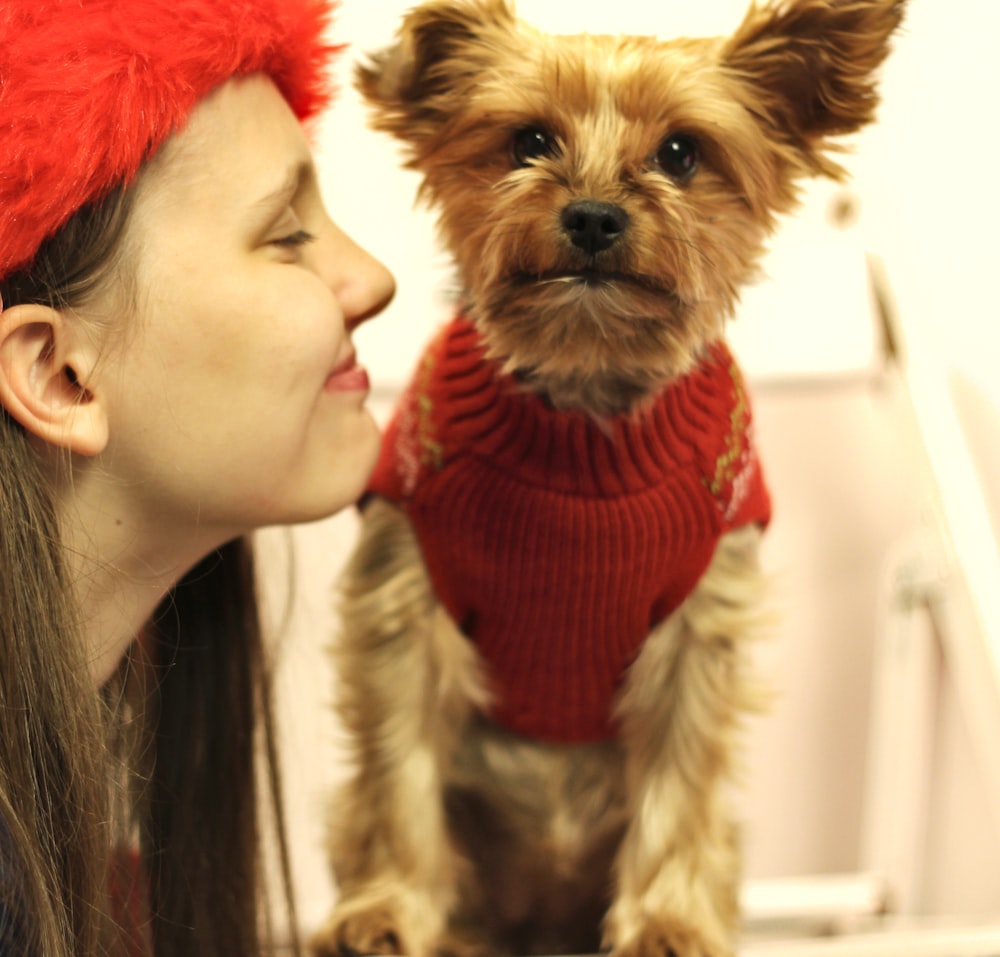 Mujer con gorra de punto roja sosteniendo Yorkshire Terrier marrón y negro