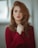 Portrait of a woman with auburn hair in red sweater holding her hands on her heart