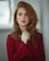 Portrait of a woman with auburn hair in red sweater holding her hands on her heart
