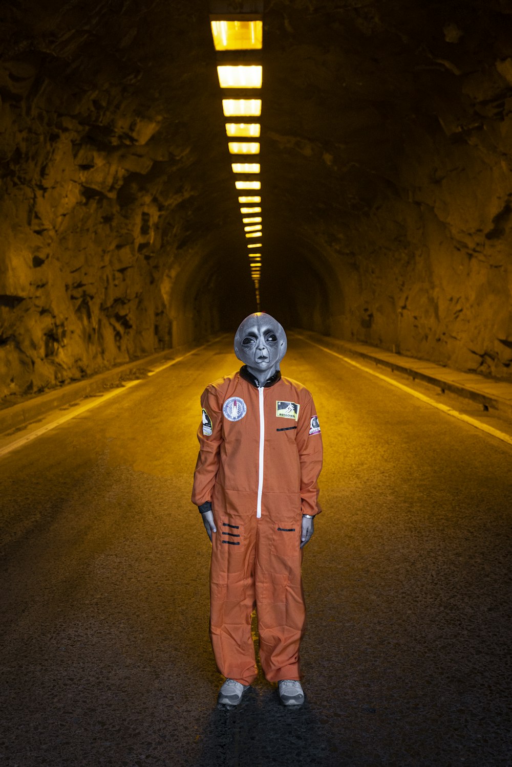 man in orange jacket wearing helmet standing on road