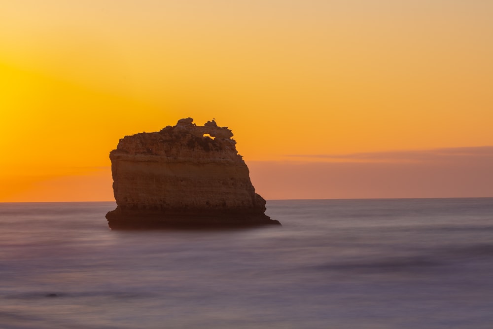 brown rock formation on body of water during sunset