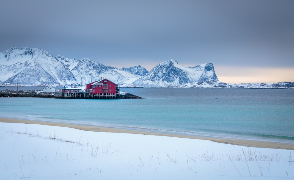 Casa Roja y Blanca cerca del cuerpo de agua y la montaña cubierta de nieve durante el día