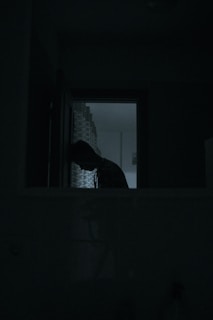 Shadowy silhouette of a man standing alone in a dark, empty room
