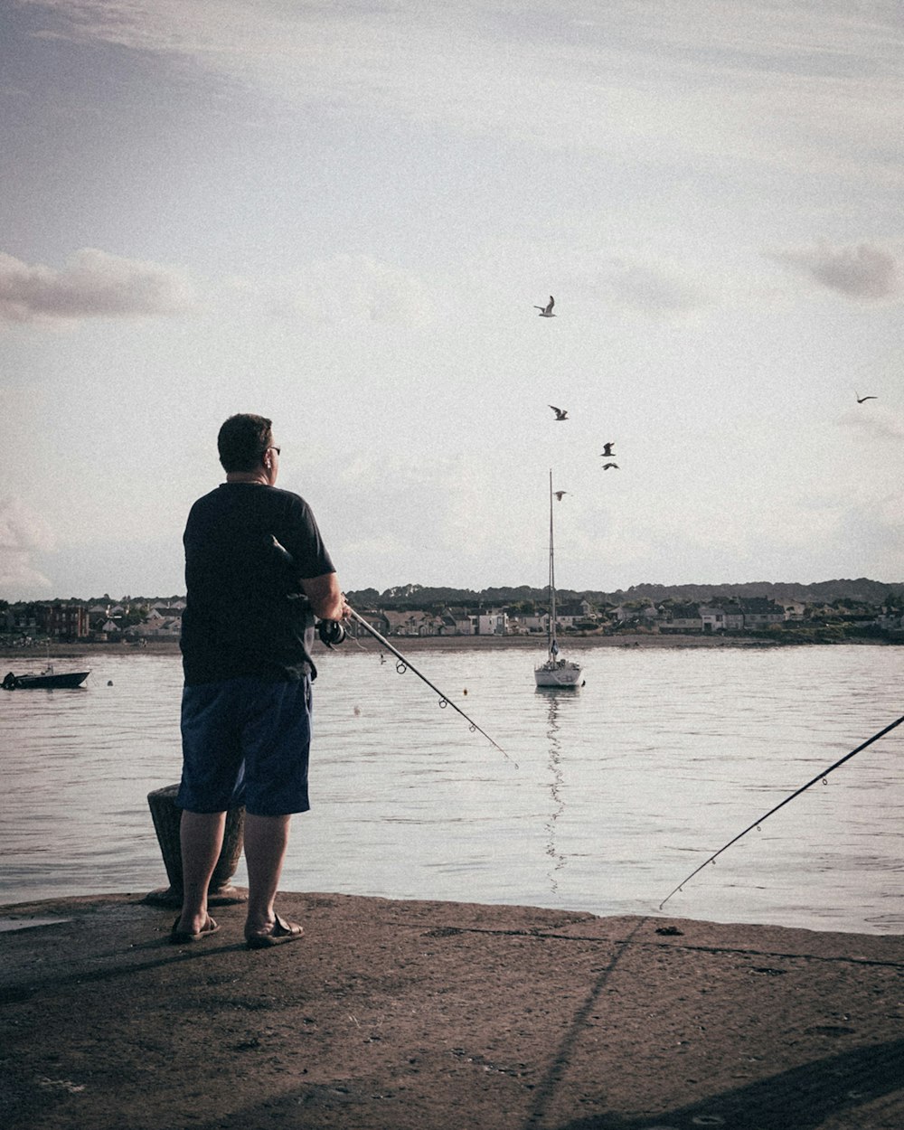 man in black shirt and blue shorts fishing on lake during daytime