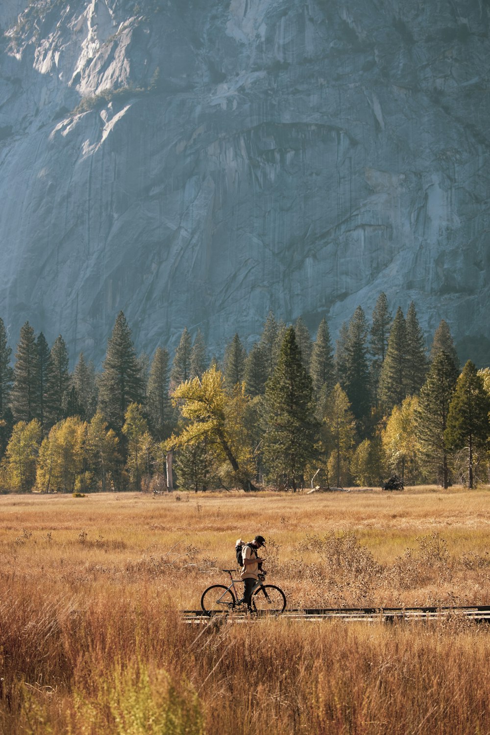 man riding bicycle on brown grass field near green trees and mountain during daytime