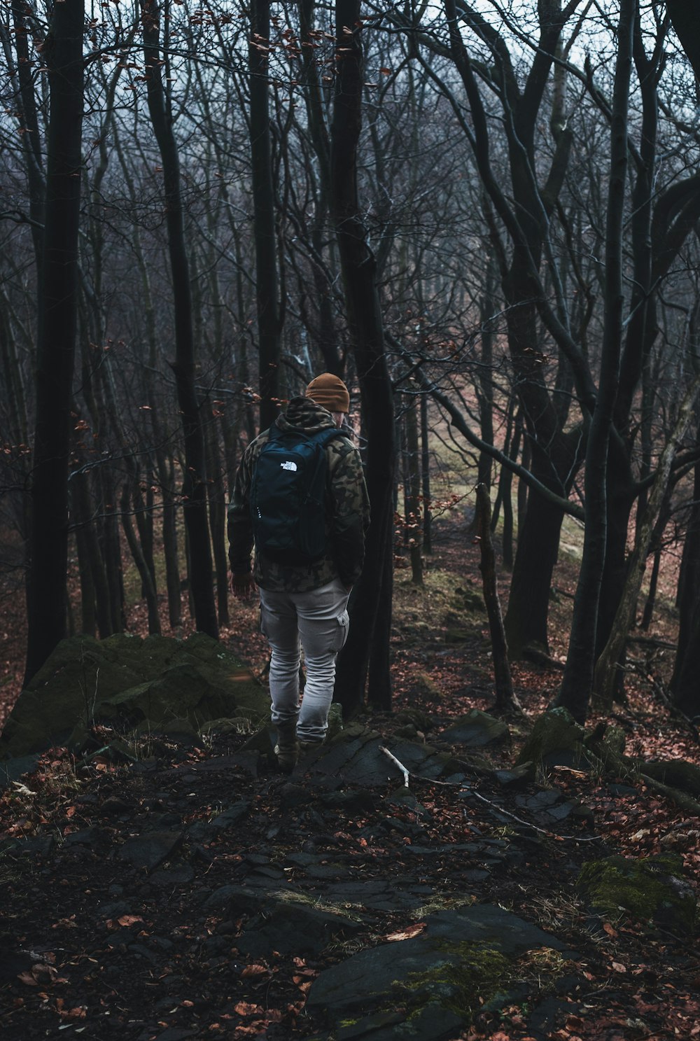 Hombre con chaqueta negra y pantalones blancos de pie en medio del bosque