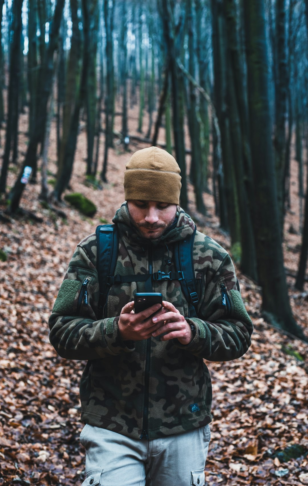 man in green and black camouflage jacket holding black smartphone