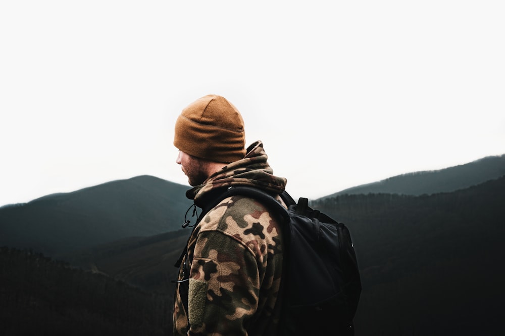 man in black jacket and brown knit cap standing on top of mountain during daytime