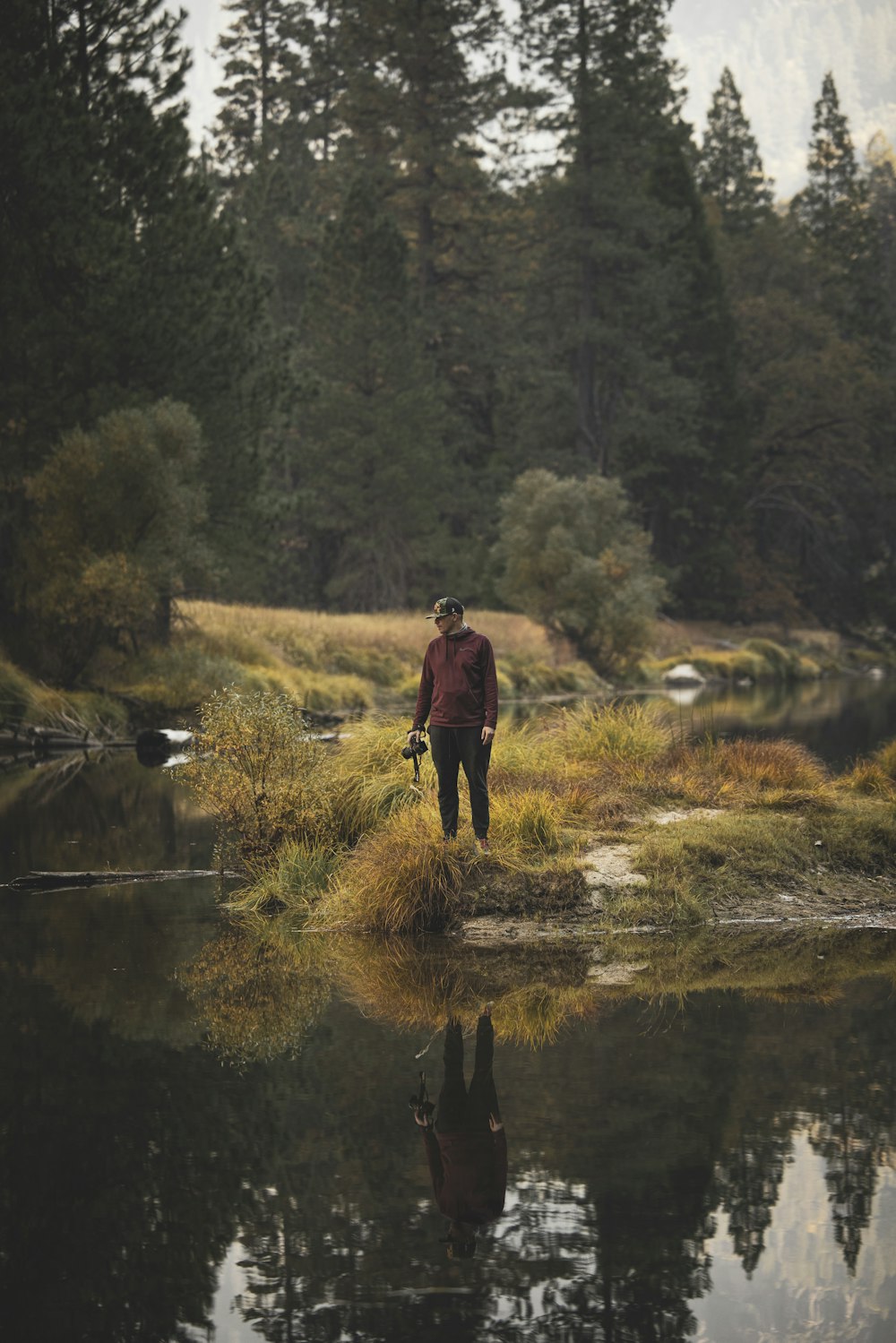 man in black jacket and black pants walking on green grass field near river during daytime